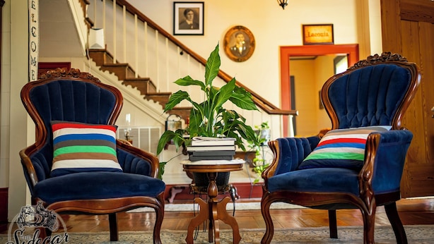 Une pièce avec deux fauteuils bleu foncé, recouverts d’un tissu d’ameublement, agrémentés de coussins à rayures, une petite table ronde sur laquelle est posée une plante en pot, et un escalier en arrière-plan.