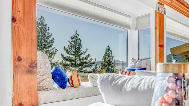 Un salon moderne doté d’une grande fenêtre donnant sur un paysage de arbres et de montagnes.