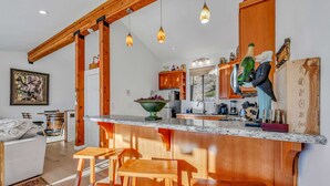Une cuisine moderne agrémentée d’éléments en bois, un coin bar avec des tabourets et un espace repas avec un canapé blanc.