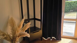 Una stanza con un tavolino nero alto e stretto, una pianta in vaso con pannocchie di pampa secche, una tenda scura e vista su uno spazio esterno attraverso una porta di vetro.