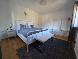 A bedroom with a bed, bedside tables, a mirror, a deer head decoration, a bench, and a window.