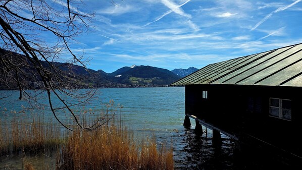 Une cabane en bois au bord d’un lac, avec des montagnes en arrière-plan.
