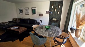 Ein modernes Wohnzimmer mit einer schwarzen Couch, einem runden Marmortisch und einer grünen Schale, sowie einem an der Wand befestigten Fernseher.