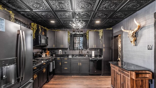 A modern kitchen with black cabinetry, stainless steel appliances, and a wooden floor.