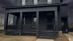 A two-story black house with a porch, a front door, and a mailbox.