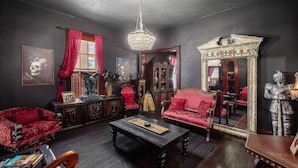 A room with a chandelier, red upholstered furniture, a vintage cabinet, and a large mirror.
