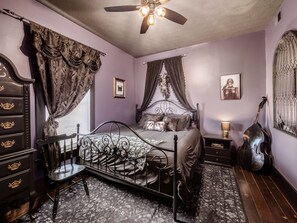 Ein Schlafzimmer mit Bett, Kommode, Stuhl, Gitarre und Deckenventilator.