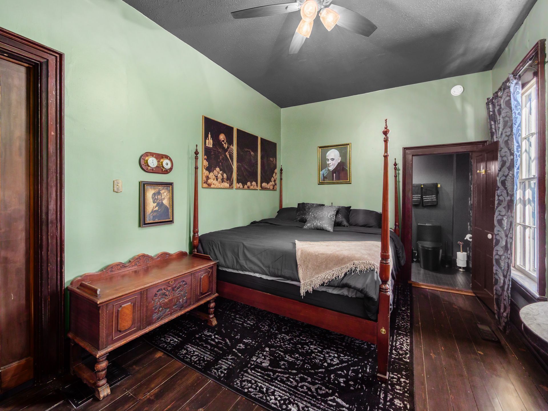 Une chambre à coucher avec un lit à baldaquin, une table de chevet en bois, un tapis à motifs noir et blanc et un ventilateur de plafond.