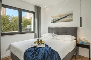 Ein modernes Hotelzimmer mit einem großen Bett, Blick auf die Stadt und einem Bild an der Wand.