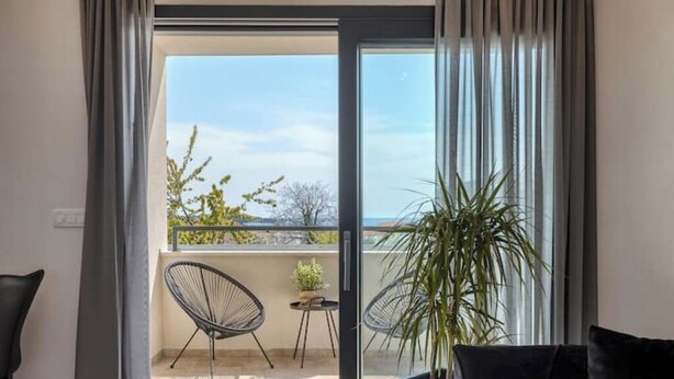 En balkon med udsigt over havet, en potteplante og to stole.