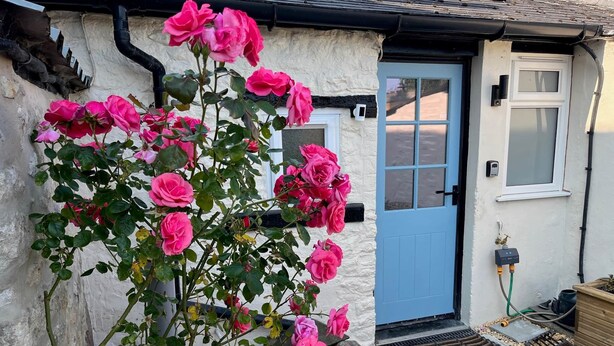 A rustic house with a blue door, a rose bush in front, and a small garden area. - Arcadia - 2-Bed, Dog Friendly with EV Charger (Mere)