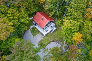 Eine zweistöckige Holzhütte mit rotem Dach, umgeben von dichtem Wald.