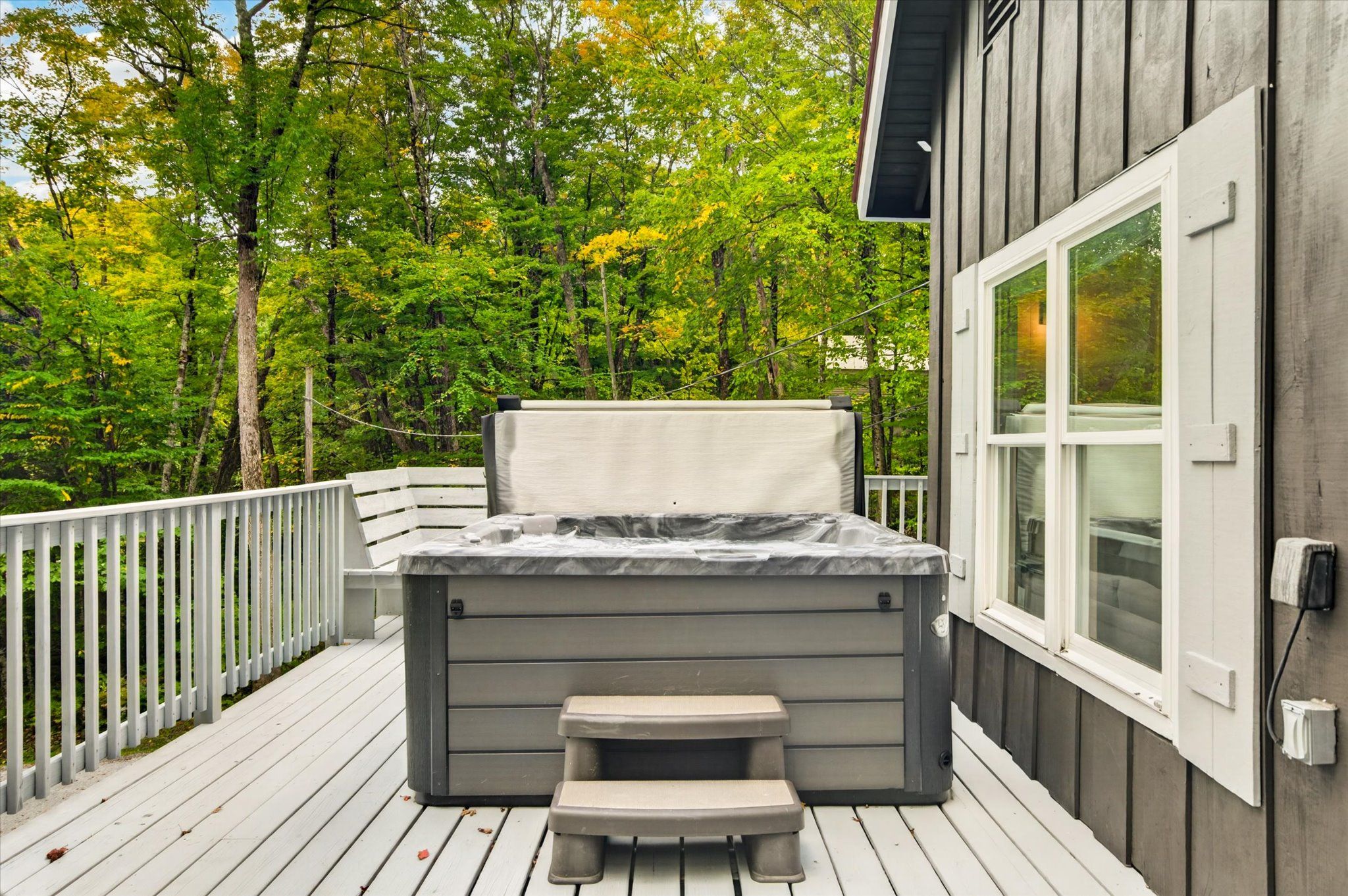 A hot tub on a wooden deck with a view of a forest.