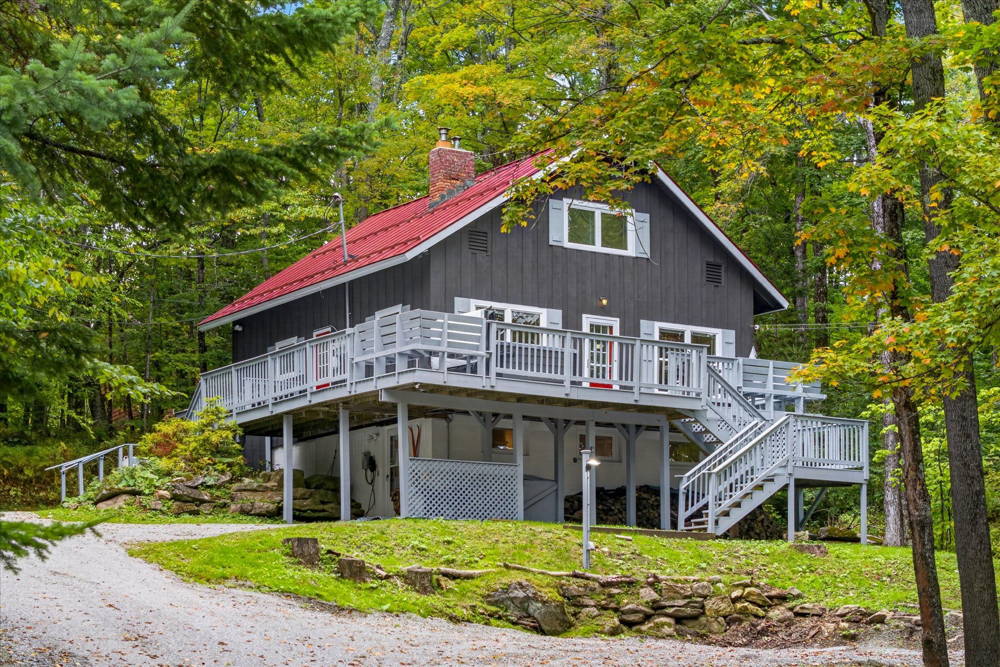 A two-story cabin with a red roof, a balcony, and a staircase leading to the upper level.