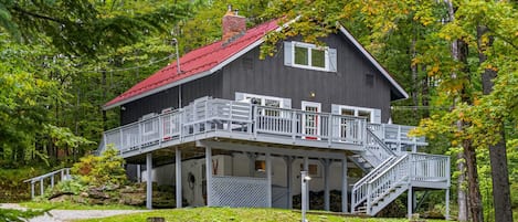 A two-story cabin with a red roof, a balcony, and a staircase leading to the upper level.