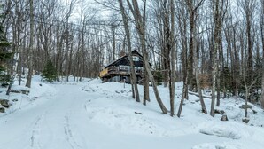 A cabin in a snowy forest with a dirt path leading to it. - Vermont Mountain Escape – Spacious Duplex with Privacy & Amenities (Killington)