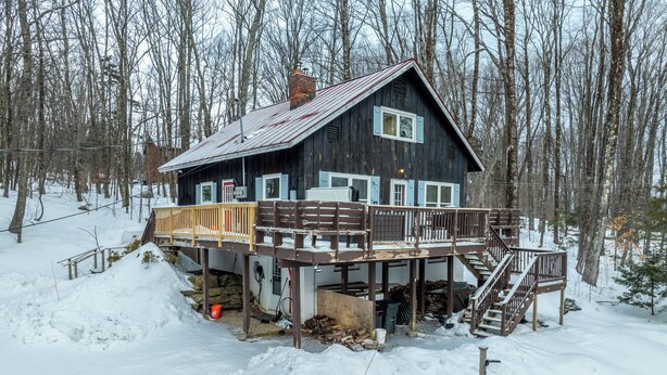 A wooden cabin with a deck and stairs, surrounded by snow and trees. - Vermont Mountain Escape – Spacious Duplex with Privacy & Amenities (Killington)