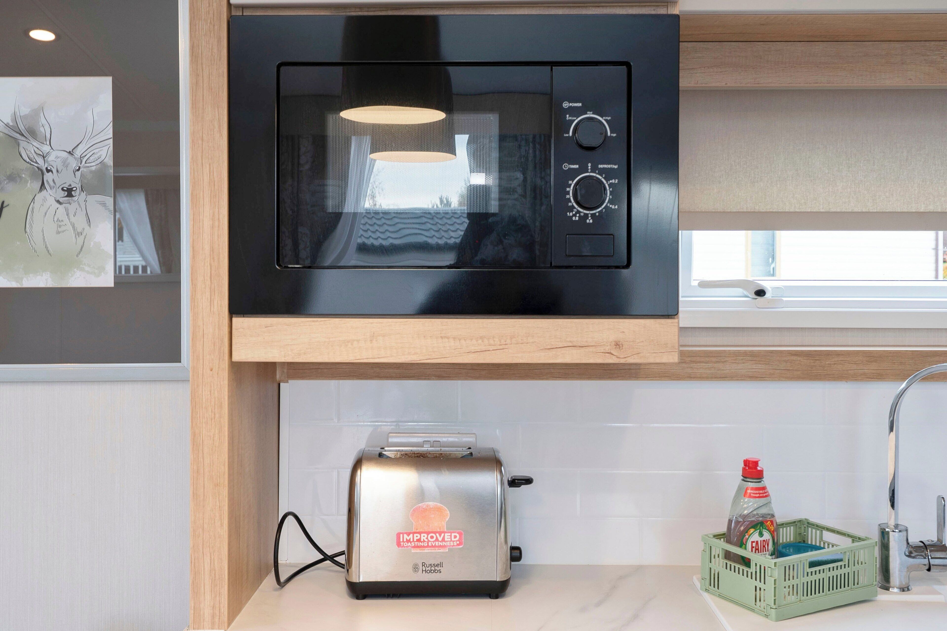 A kitchen with a modern microwave, toaster, and a green crate with a bottle.