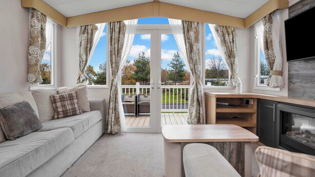Ein gemütliches Wohnzimmer mit einer Couch, einem Couchtisch und einem Kamin. Es gibt einen Balkon mit Blick auf Bäume und eine Terrasse.