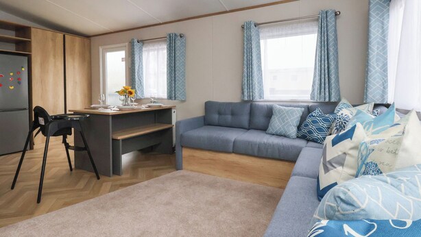 Un espacio habitable compacto con kitchenette, un sofá, una mesa de comedor y una ventana con cortinas.