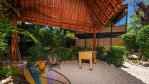 Een terras met rieten stoelen en een houten tafel, omringd door weelderige begroeiing en een houten pergola.