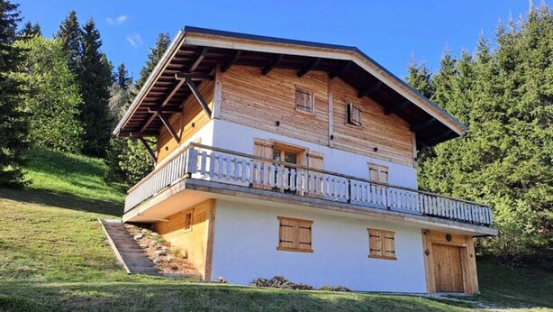 En tvåvånings chalet med en träbalkong, en trappa som leder upp till entrén och en omgivande skog.