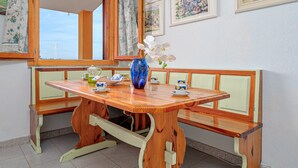 Een houten eettafel met een bankje, een vaas met witte bloemen en een raam met gordijnen.