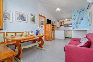 Een eethoek met een houten tafel en banken, een keuken op de achtergrond en een rode bank op de voorgrond.