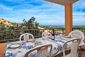 A balcony with a table set for dining, chairs, and a view of the sea and hills. - Apartment 'Quadrilocale Le Colonne' with Sea View, Private Terrace and Air Conditioning (Li Mori)