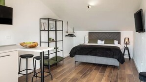 Une chambre à coucher moderne, avec un lit, un bureau doté de tabourets, une bibliothèque et un téléviseur fixé au mur.