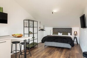 A modern bedroom with a bed, a desk with stools, a bookshelf, and a TV mounted on the wall. - Soulshine Belvedere Holidays – Modern Studio with Adriatic Views & Terrace (Novigrad)