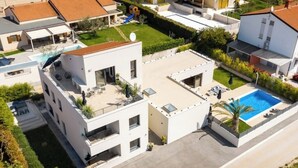 Un immeuble résidentiel moderne à plusieurs étages, doté d’une terrasse sur le toit, d’une piscine et d’un jardin bien entretenu.