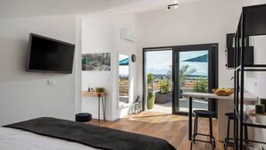 Une chambre d’hôtel moderne équipée d’un lit, d’un téléviseur fixé au mur, d’un balcon offrant une vue sur la ville et d’un petit coin cuisine.