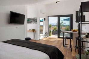 A modern hotel room with a bed, a TV mounted on the wall, a balcony with a view of the city, and a small kitchen area. - Soulshine Belvedere Holidays – Modern Studio with Adriatic Views & Terrace (Novigrad)