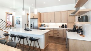 A modern kitchen with a central island, bar stools, wooden cabinets, and stainless steel appliances. - Spacious Retreat II Fireplace, Hot Tub, Free Bus, 2 Master Bedrooms (Fraser)