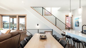 A modern kitchen with a wooden table, bar stools, and a staircase leading to an upper level. - Spacious Retreat II Fireplace, Hot Tub, Free Bus, 2 Master Bedrooms (Fraser)
