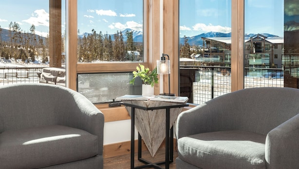 A balcony with two grey armchairs, a small table with a plant, and a view of a snowy mountain landscape. - Spacious Retreat II Fireplace, Hot Tub, Free Bus, 2 Master Bedrooms (Fraser)