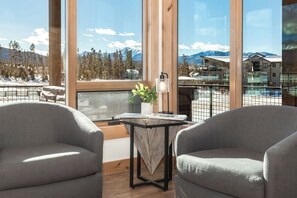 A balcony with two grey armchairs, a small table with a plant, and a view of a snowy mountain landscape. - Spacious Retreat II Fireplace, Hot Tub, Free Bus, 2 Master Bedrooms (Fraser)