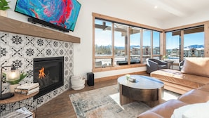 A modern living room with a fireplace, a television, and a large window offering a mountain view. - Spacious Retreat II Fireplace, Hot Tub, Free Bus, 2 Master Bedrooms (Fraser)