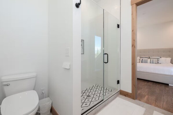 A modern bathroom with a glass shower enclosure, a white toilet, and a visible tiled floor. - Spacious Retreat II Fireplace, Hot Tub, Free Bus, 2 Master Bedrooms (Fraser)