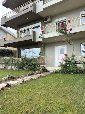 A multi-story residential building with balconies, a central air conditioning unit, and a well-maintained garden with rocks and flowering plants.