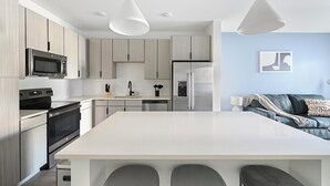 A modern kitchen with a central island, stainless steel appliances, and light wood cabinetry. - Landing | Modern 1BD, Yoga Studio, Gym (Perdido Key)