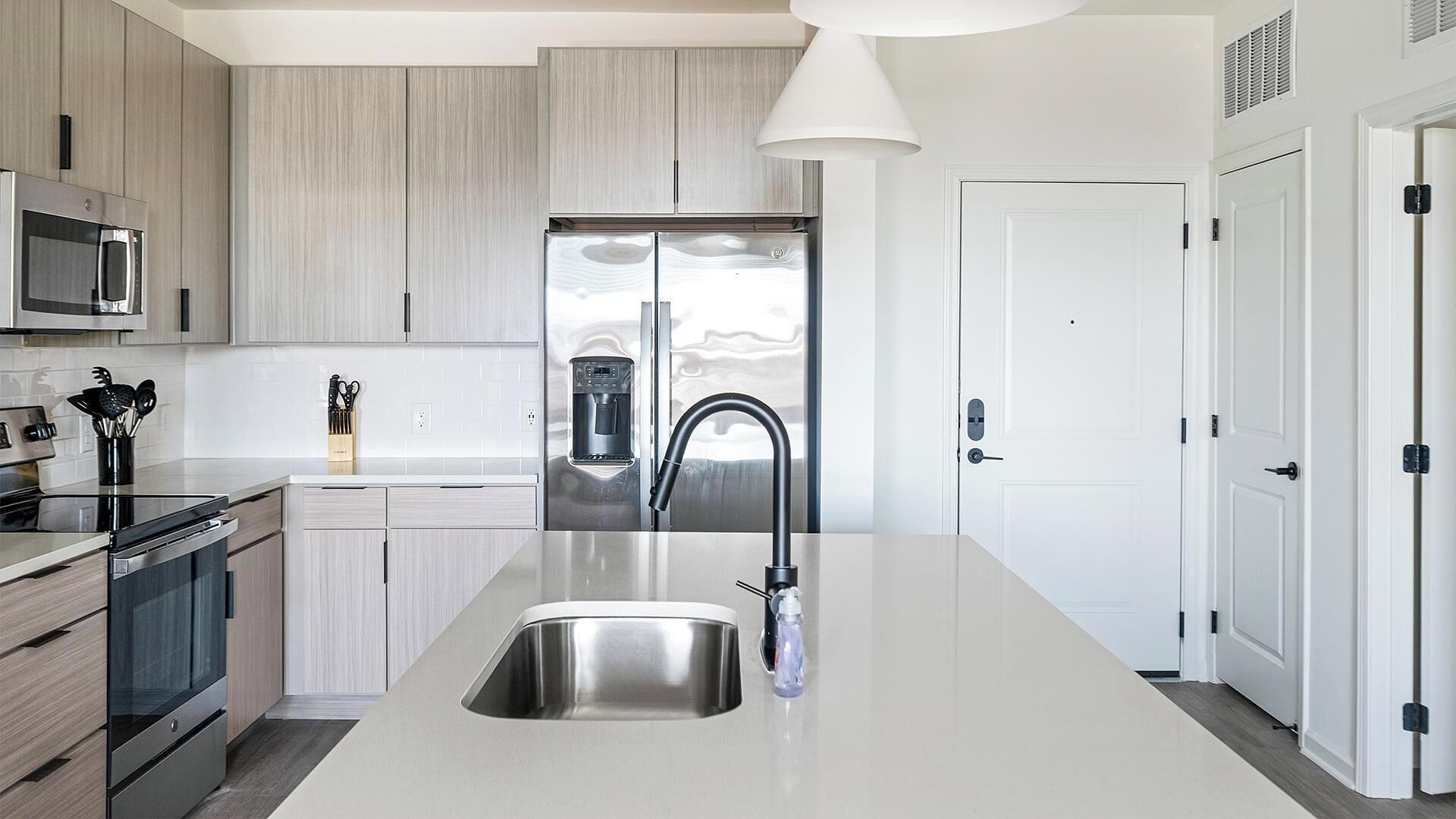 A modern kitchen with a stainless steel sink, a built-in microwave, and a water dispenser.