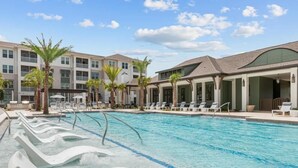 A swimming pool with lounge chairs and palm trees, surrounded by multi-story buildings with balconies. - Landing | Amazing 1BD, Gym, Clubhouse (Perdido Key)