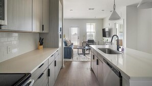 A modern kitchen with a central island, a dining area with a table and chairs, and a view of the city through large windows. - Landing | Amazing 1BD, Gym, Clubhouse (Perdido Key)