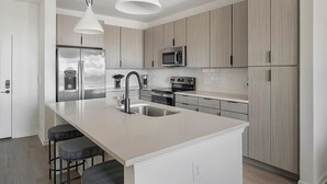 A modern kitchen with a central island, stainless steel appliances, and light wood cabinetry. - Landing | Amazing 1BD, Gym, Clubhouse (Perdido Key)