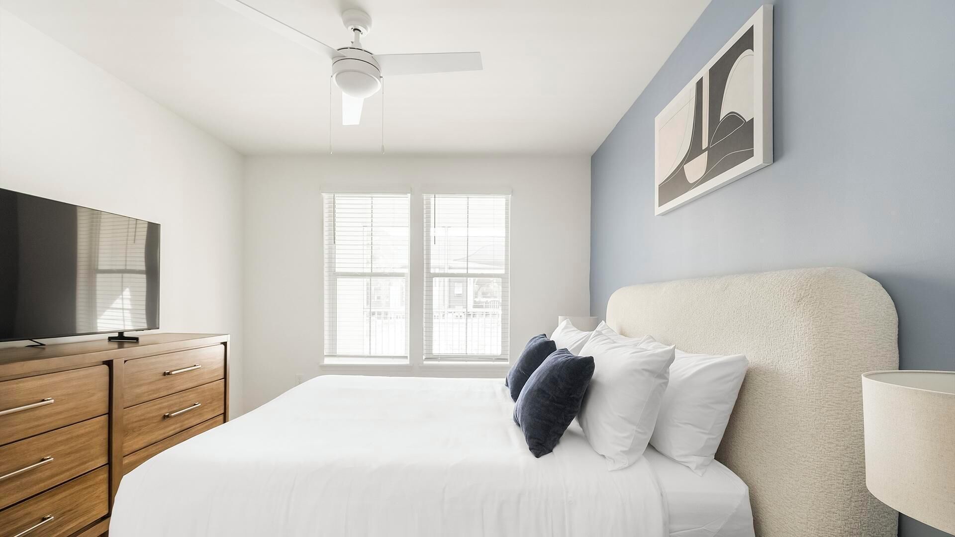 Un dormitorio con cama, televisor, ventilador de techo y ventana.