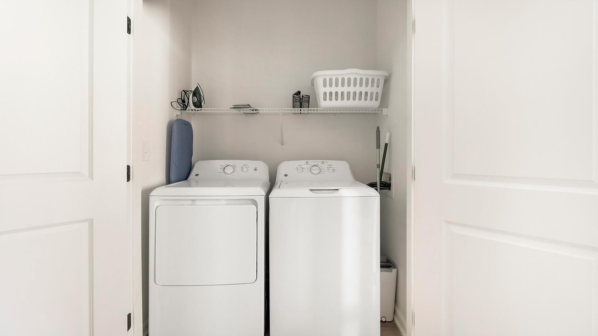 Une buanderie équipée de deux machines à laver à chargement frontal blanches et d’un panier à linge blanc posé sur une étagère.