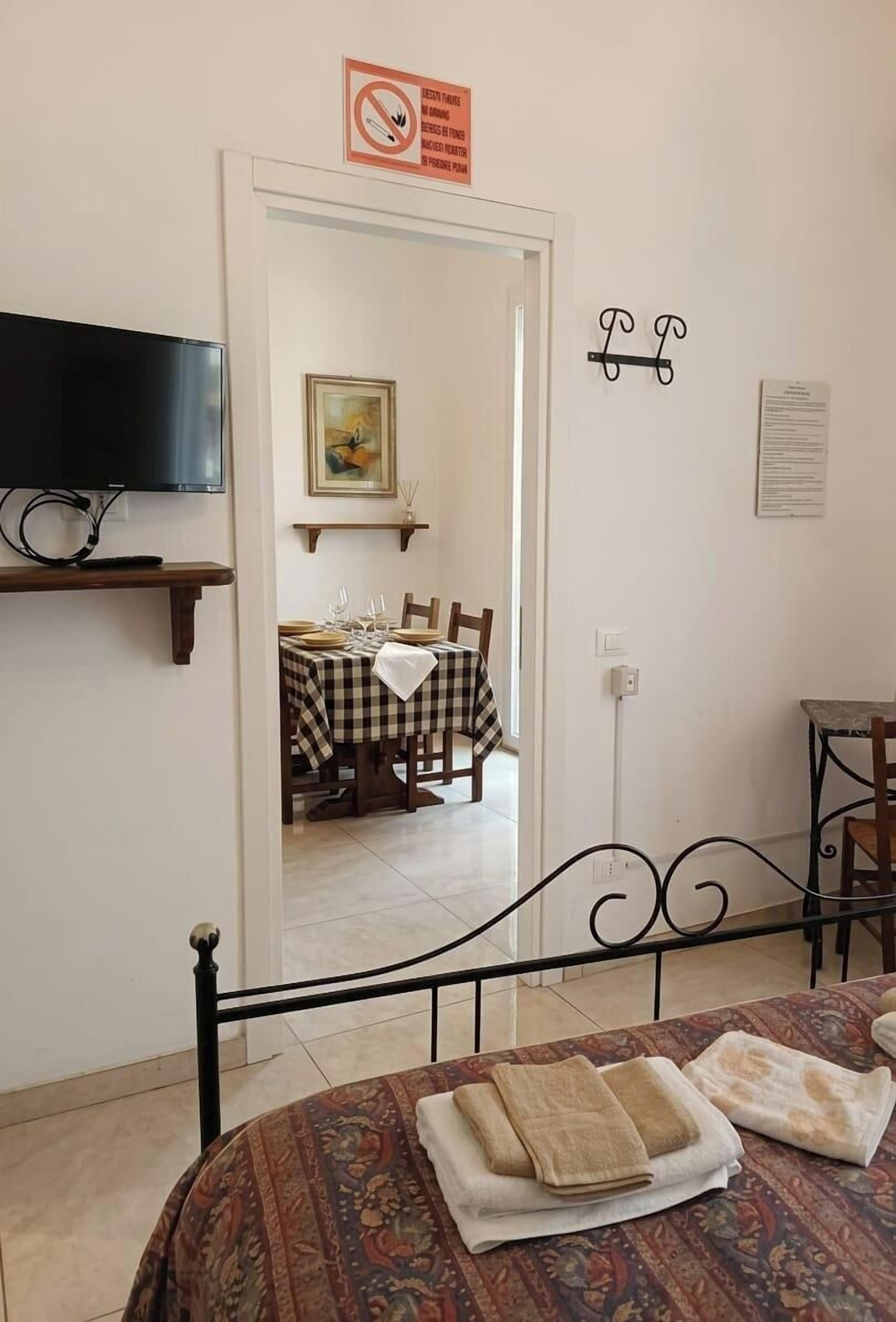 A room with a bed, a TV, a dining table with chairs, and a painting on the wall.