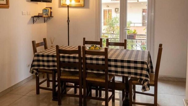 A dining area with a checkered tablecloth, wooden chairs, a television on the wall, and a window with a view of a building. - Laura's little houses: second floor 2 (Palermo)